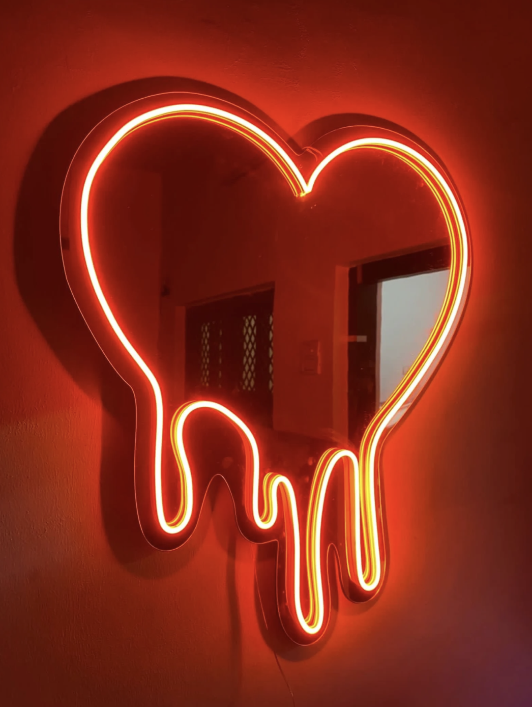 Espejo LED de corazón rojo con efecto dripping en una pared